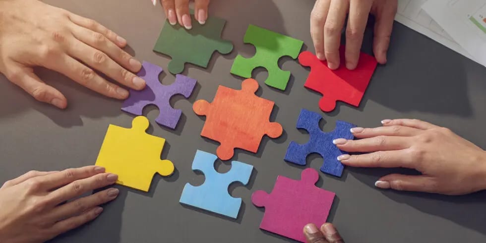 Colourful puzzle pieces being assembled by several hands
