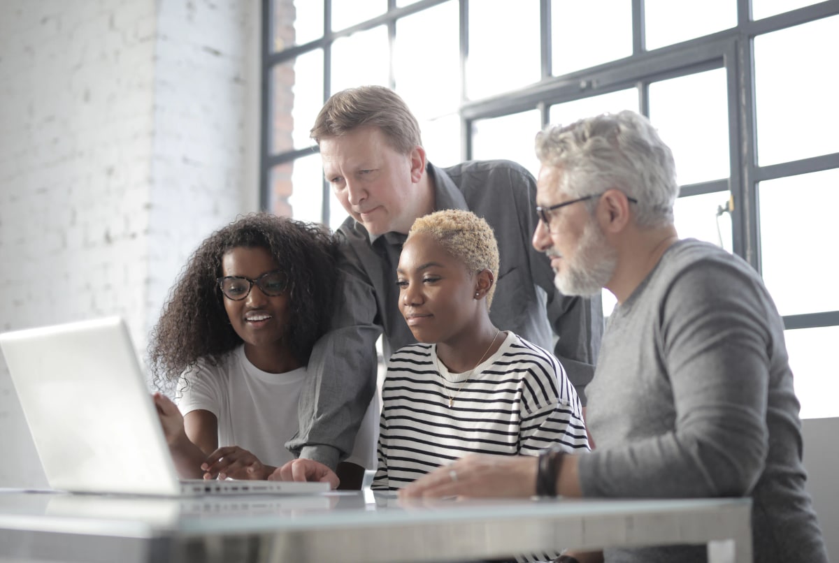 Colleagues gathered around a laptop by tall windows