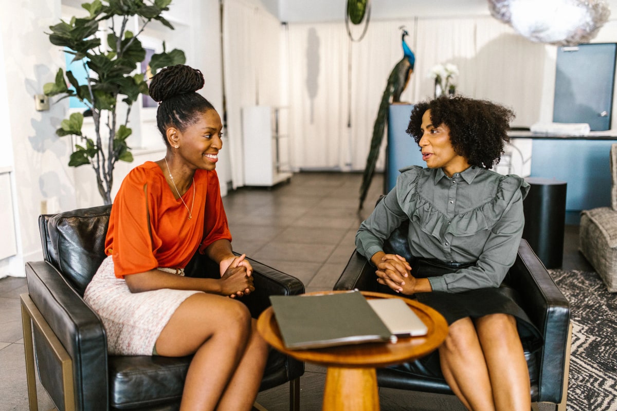 Two women smiling in a coaching conversation in armchairs in a bright office