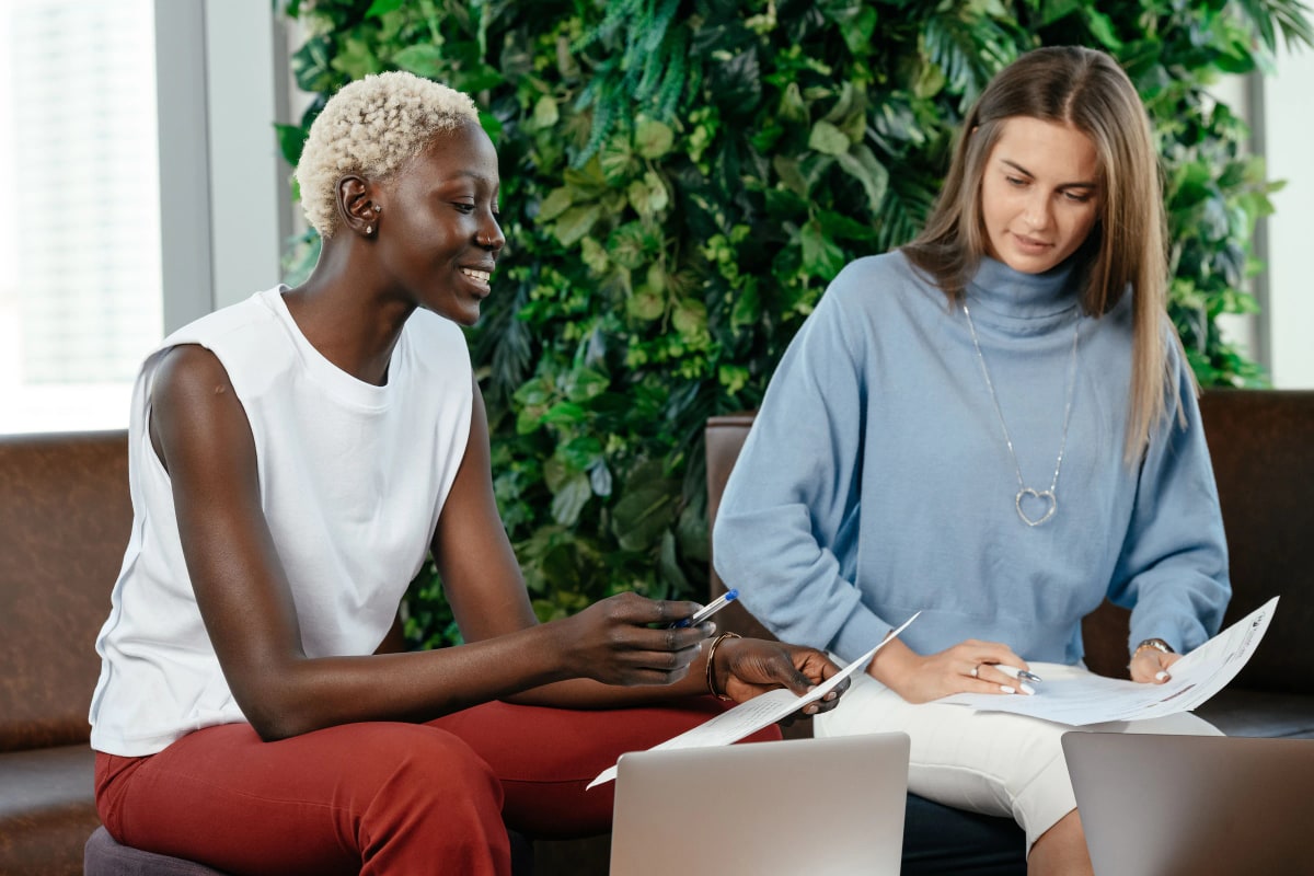 Two women going over printed notes together on a sofa